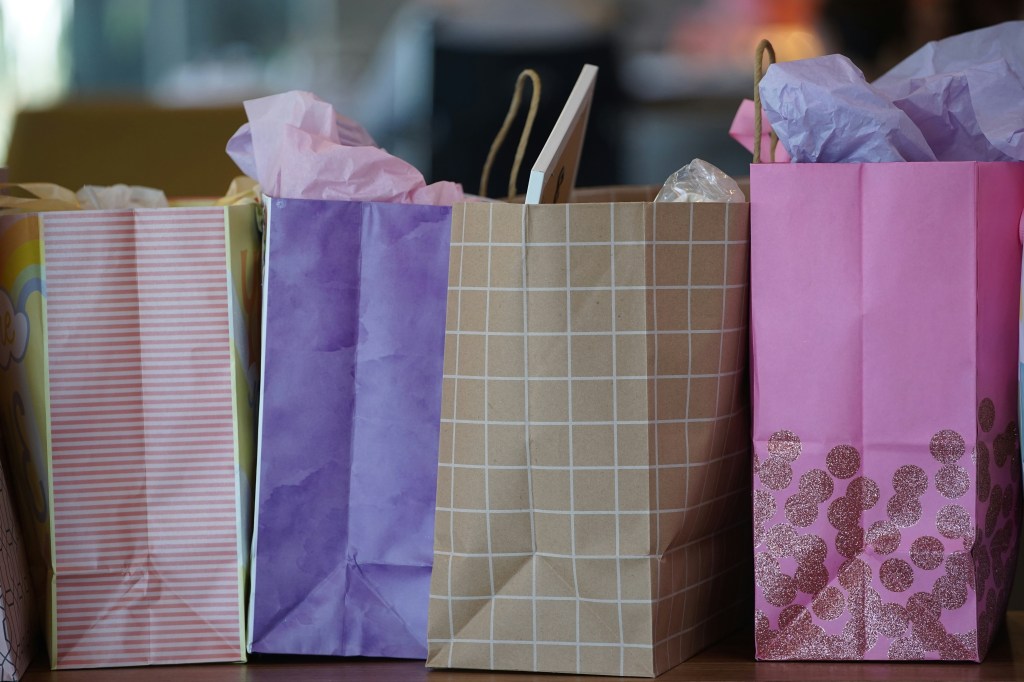Großaufnahme von vier nebeneinander stehenden, gefüllten Einkaufstüten aus Papier. Aus zweien ragen oben pastellfarbene Seidenpapiere heraus.